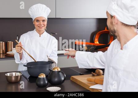 Junge lächelnde Frau Koch Kochen in modernen Interieur der privaten Küche mit männlichen Kollegen Stockfoto