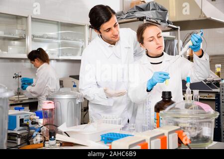 Zwei fleißigen positive Studenten führen Experimente im Labor der Universität, mit mechanischen lab Pipette für Mischen von Chemikalien Stockfoto