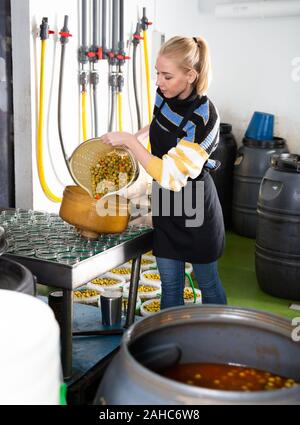 Junge workwoman füllen Gläser mit Eingelegte grüne Oliven in Verpackung Shop im Werk Stockfoto