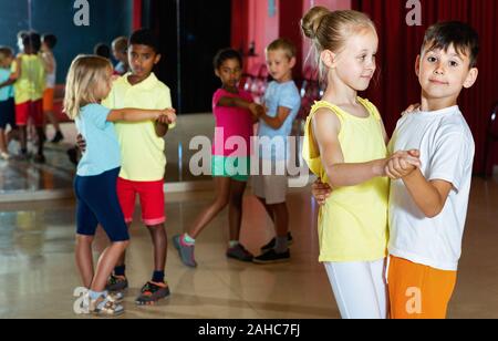Gruppe von froh lächelnde Kinder versucht, Tanzen mit Partner im Klassenzimmer Stockfoto
