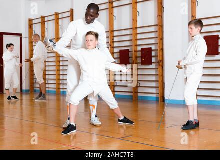 Sorgfältige ernste positive jungen Fechter aufmerksam zuhören, um professionelle fechten Trainer im Fitnessstudio konzentriert Stockfoto