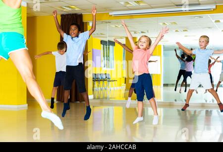 Gruppe von aktiven sportlichen Kinder mit weiblichen Lehrer Ausbildung in Modern Dance Hall, zusammen springen Stockfoto