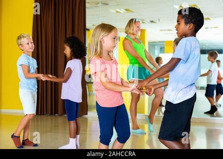 Gruppe von fröhlichen positive lächelnde Kinder üben heftige jive Bewegungen im Tanz Klasse mit weiblichen Trainer Stockfoto