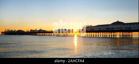 Brighton Pier, Stretching Meer bei Sonnenuntergang, die Front der Pier mit dem Namen auf, die Sonne unter der Pier bilden einen schönen Stern b Stockfoto