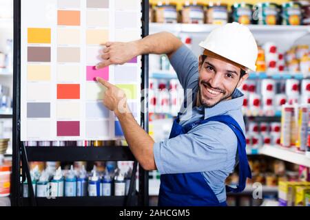 Lächelnd Vorarbeiter in blauen Overalls mit Proben von Farbe auf Stand in Store Stockfoto