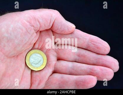 Ein britisches Pfund Münze in der Hand eines Mannes vor einem dunklen Hintergrund Stockfoto