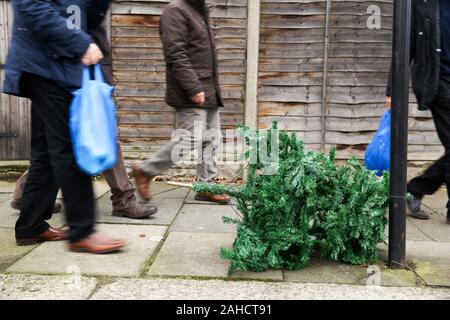 Nördlich von London, UK. 28 Dez, 2019. Shopper sind gesehen hinter einem weggeworfenen Weihnachtsbaum links auf dem Bürgersteig in Haringey, nördlich von London, nur drei Tage nach Weihnachten. Credit: Dinendra Haria/Alamy leben Nachrichten Stockfoto