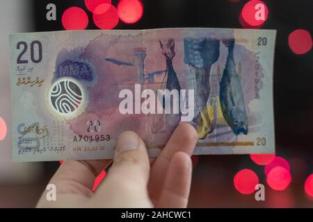 Hand hält eine Maledivische rufiyaa Bank Note Währung Geld (20), pink und rot bokeh Hintergrund mit Copyspace Stockfoto