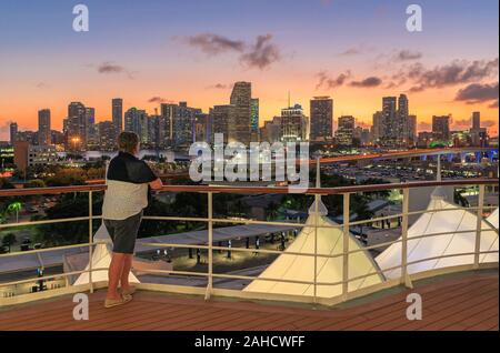 Frau mit Blick auf die Skyline von Miami nach Sonnenuntergang von einem Kreuzfahrtschiff Geländer Stockfoto