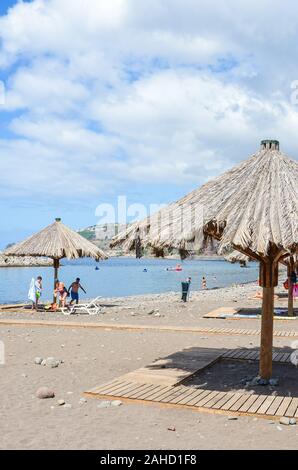 Ribeira Brava, Madeira, Portugal - Sep 9, 2019: Sandstrand im Madeira Reiseziel. Sonnenliegen und Sonnenschirmen, die Leute am Strand am Atlantischen Ozean. Sommertag. Vertikale Foto. Stockfoto