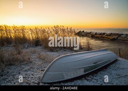 Die ersten Strahlen der Sonne über dem Ladogasee am Morgen im Winter. Eine umgeworfen Boot an einem verschneiten Strand. Region Leningrad. Stockfoto