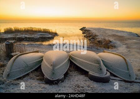 Die ersten Strahlen der Sonne über dem Ladogasee am Morgen im Winter. Umgeworfen Boote an einem verschneiten Strand. Region Leningrad. Stockfoto