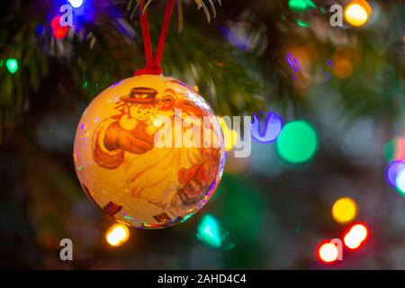 Hand-made Christbaumkugel hängt am Ast eines Weihnachtsbaum mit unscharf Lichterketten in den Hintergrund