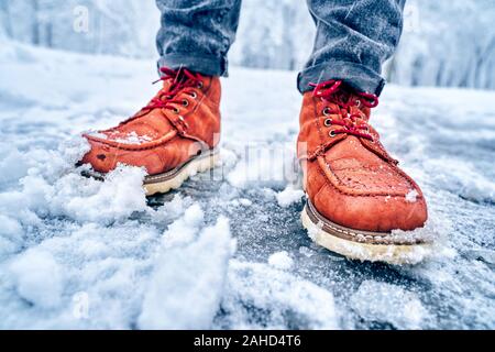 Füße eines Mannes auf eine schneebedeckte Bürgersteig in braune Stiefel. Winter rutschig pawement. Saisonale wetter Konzept Stockfoto