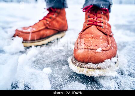 Füße eines Mannes auf eine schneebedeckte Bürgersteig in braune Stiefel. Winter rutschig pawement. Saisonale wetter Konzept Stockfoto