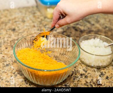 Hand Schaufeln shredded Cheddar Käse aus servierschüssel Stockfoto