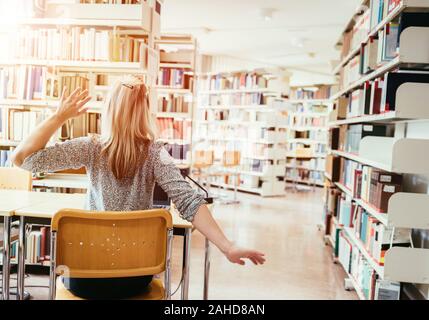 Müde Studentin sitzt am Schreibtisch mit einem Stapel Bücher, Universitätsbibliothek Stockfoto