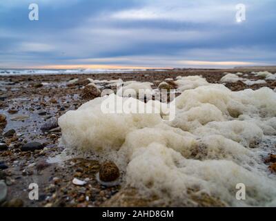 Seafoam Close-up auf einem Kies- und Sandstrand Stockfoto