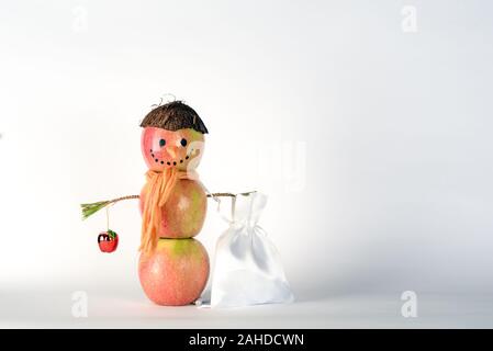 Konzept der Nachhaltigen, Null Abfall, Sommer vegane Weihnachten. Kreative Schneemann aus Äpfeln in einen Hut aus Kokosnuss holding Geschenk Sack voller Geschenke für Weihnachten auf weißem Hintergrund. Stockfoto