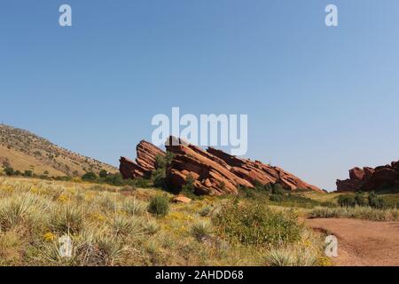 Eine rote Schmutz weg vorbei an wildflower Wiesen und rote Felsformationen ragt aus dem Boden auf der Trading Post Trail im Red Rock State Park, C Stockfoto