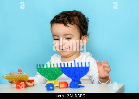 Jüdischen Jungen spielen mit festlichen Hanukkah festliche Hanukkah Menorah Blau und Grün und bunt Holz Dreidels. Selektiver Fokus auf Kind. Stockfoto