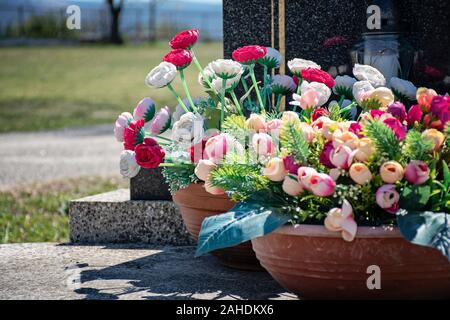 Friedhof in sonniger Tag. Grabstein mit Blumen und Kerzen. Grab Dekoration close-up. Friedhof in der Tageszeit. Grab Blumen im Topf. Stockfoto