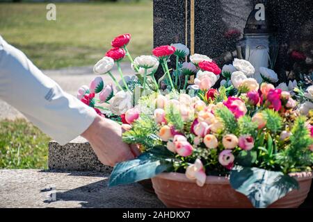 Friedhof in sonniger Tag. Grabstein mit Blumen und Kerzen. Grab Dekoration close-up. Friedhof in der Tageszeit. Grab Blumen im Topf. Stockfoto