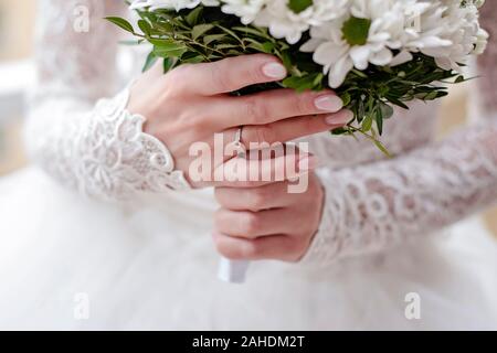 Braut im weißen Kleid ist Holding Hochzeit Blumen. Close-up für die Braut Hände tragen Engagement Ring und weißer Blumenstrauß. Stockfoto