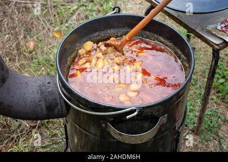 Kochen köstliches Kesselgulasch mit Treffen, Pfeffer, Tomaten, Zwiebel in einem großen Topf im Freien Stockfoto