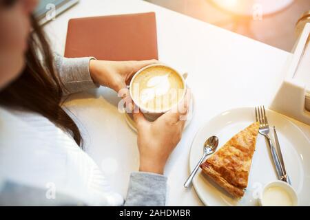 Junge lächelnde Frau tun einer Kaffeepause im Cafe sitzen, mit Notebook und Tasse Kaffee oder Latte, Spinatkuchen, Ansicht von oben. Stockfoto