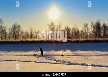 Silhouette eines einsamen Angler auf einem schneebedeckten Fluss, im Licht der aufgehenden Sonne Stockfoto