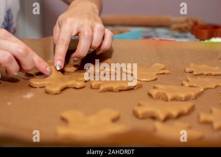 Weibliche Hände ausbreiten, den Teig in die Form eines Mannes, auf Backpapier. Der Prozess der Herstellung Weihnachtsplätzchen. Selektive konzentrieren. Stockfoto