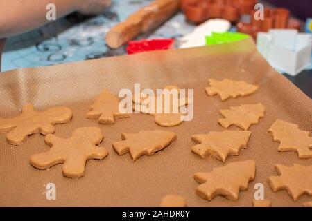 Rohen Teig in Form Lebkuchen Cookies der Weihnachtsbäume und wenig Männer liegen auf Backpapier close-up. Selektive konzentrieren. Im Hintergrund paraphern Stockfoto