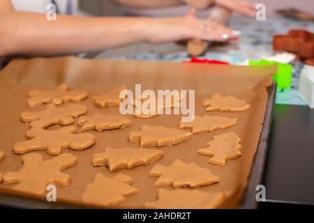 Rohen Teig in Form Lebkuchen Cookies der Weihnachtsbäume und wenig Männer liegen auf Backpapier close-up. Selektive konzentrieren. Im Hintergrund, weiblich h Stockfoto