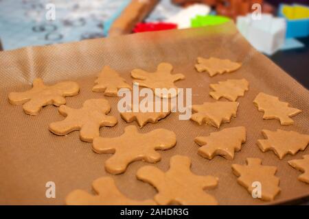 Rohen Teig in Form Lebkuchen Cookies der Weihnachtsbäume und wenig Männer liegen auf Backpapier close-up. Selektive konzentrieren. Im Hintergrund paraphern Stockfoto