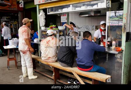 Kunden (darunter zwei Metzger) Essen in Essen stand in Paloquemao Markt, Bogota, Kolumbien Stockfoto