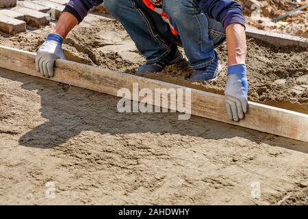 Ein Arbeitnehmer, der Ebenen der sand Stiftung mit einem hölzernen Ebene fortzusetzen verlegen Pflastersteine, Bild mit Kopie Raum, Bild mit kopieren. Stockfoto