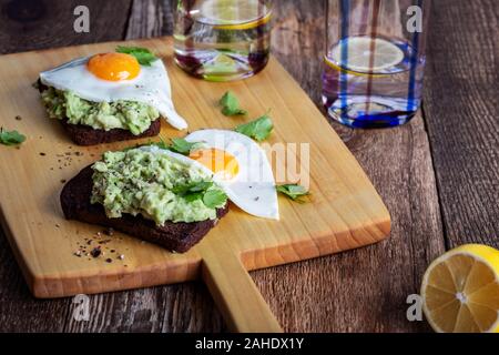 Frühstück oder Brunch am Valentinstag, Avocado Roggen Brot Toast mit Spiegelei serviert wird auf rustikalen Holzbrett, gesunde, vegetarische Mahlzeit für zwei Personen Stockfoto