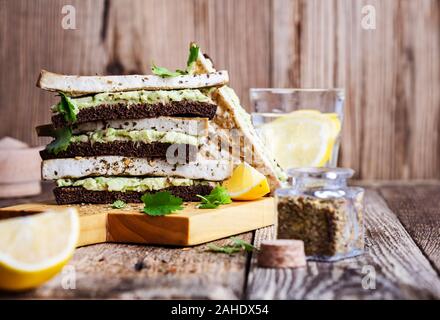 Frühstück oder Brunch, Avocado Roggen Brot Toast mit gegrillten herbed Tofu, auf pflanzlicher Basis Snack auf rustikalen Holzbrett serviert gesunde vegane Mahlzeit Stockfoto