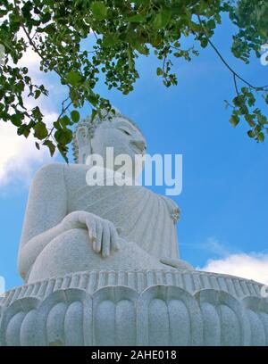 Riesige Marmor statue des Sitzenden Buddha in Phuket, Thailand. Low Angle View mit Blättern im Vordergrund. Stockfoto