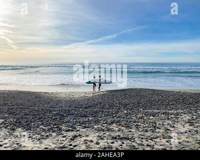 Surfer gehen mit ihren Brettern auf Torrey Pines State Beach vor Sonnenuntergang Dämmerung, Küsten Strand in San Diego, Kalifornien entfernt. Dezember 12th, 2019 Stockfoto