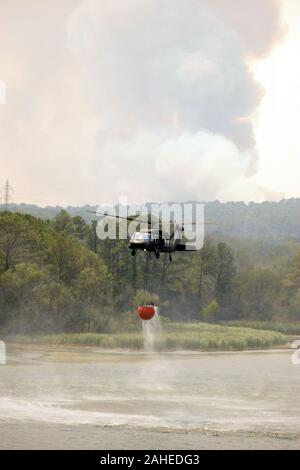 Ein Texas National Guard UH-60 Black Hawk Köpfe zurück zu Schlacht die Flamme in den Hintergrund, nachdem es seine Antenne Lieferung Eimer Wasser in der Nähe von Falmouth, Texas, Sept. 6, 2011 Nachfüllungen. Texas National Guard Mannschaften gestartet aus dem Austin Army Aviation Standort wilde Brände zu bekämpfen. Sie sind Teil einer interinstitutionellen Reaktion, das US-Landwirtschaftsministeriums Forest Service, der bei Bedarf fliegen Beobachtungsmissionen Antenne wildfire Löscharbeiten zu leiten. Seit 1975, dem US-Landwirtschaftsministerium und das Innenministerium haben eine interinstitutionelle Vereinbarung mit der Abteilung der Def Stockfoto