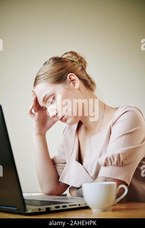 Müde, hübsche junge Frau mit Kopfschmerzen nach Arbeiten am Laptop den ganzen Tag lang Stockfoto
