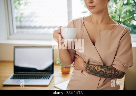 Zugeschnittenes Bild der jungen Frau, die kurze Pause und genießen Tasse Tee nach Arbeiten am Laptop zu Hause Stockfoto
