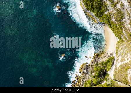 Ansicht von oben, beeindruckende Luftaufnahme von Grünem Kalkstein mit einer schönen wilden Strand vom türkisfarbenen Meer gebadet. Nusa Penida, Indonesien. Stockfoto