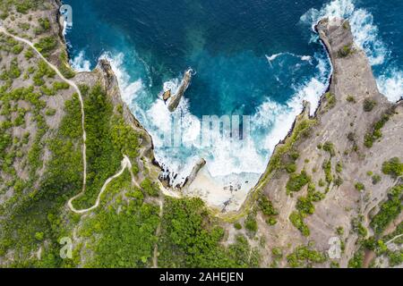 Ansicht von oben, beeindruckende Luftaufnahme von Grünem Kalkstein mit einer schönen wilden Strand vom türkisfarbenen Meer gebadet. Nusa Penida, Indonesien. Stockfoto