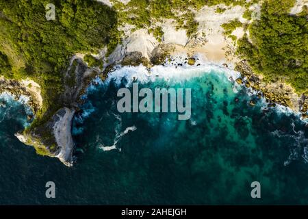 Ansicht von oben, beeindruckende Luftaufnahme von Grünem Kalkstein mit einer schönen wilden Strand vom türkisfarbenen Meer gebadet. Nusa Penida, Indonesien. Stockfoto