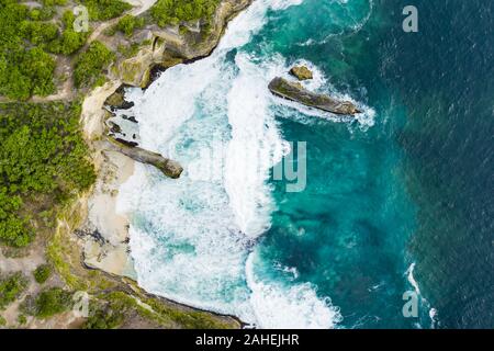 Ansicht von oben, beeindruckende Luftaufnahme von Grünem Kalkstein mit einer schönen wilden Strand vom türkisfarbenen Meer gebadet. Nusa Penida, Indonesien. Stockfoto