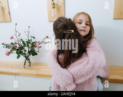 Zwei kleine Mädchen in rosa gestrickte Pullover umarmen in einem Korridor Stockfoto