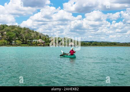 El Remate, Peten, Guatemala - 29 Mai 2019: Fischer im Kanu boot in türkisfarbenen See Itza Rudern in Richtung Dorf mit sonnigen Cloud Sky Stockfoto